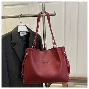 Detail view of burgundy tote bag with silver hardware on a black blazer with white background
