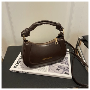 Detailed view of dark brown moon bag with twisted handle and golden hardware on a magazine