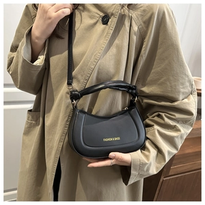 Detail of black crescent handbag with gold lettering and knotted handle on a beige trench coat
