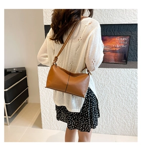 Close-up of brown leather underarm bag with decorative black stitching and knotted strap