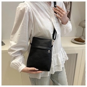 Vertical black lychee grain crossbody bag shown on model in a cozy indoor setting