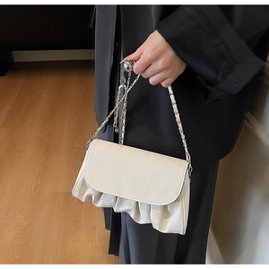 Détail d'un sac nuage plissé blanc crème avec chaîne argentée porté par un mannequin
