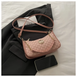 Détail d'un sac demi-lune rose poudré avec motif M et chaîne dorée sur blazer noir