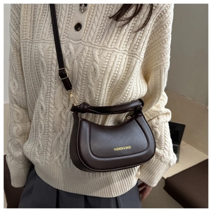 Detail of dark brown crescent crossbody bag with knotted handle on cream cable knit sweater