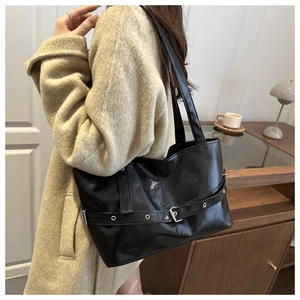 Detail of minimalist black faux leather shoulder bag with silver buckle and grommet strap