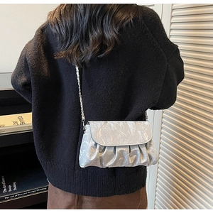 Detailed view of silver metallic pleated crossbody bag with elegant chain strap on shoulder