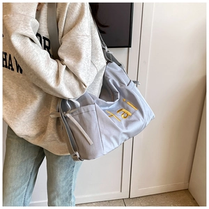 Detail of light blue-gray nylon tote bag with golden embroidered letters and side drawstring