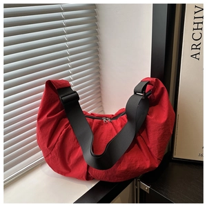 Detail of red nylon crescent shoulder bag with black strap and metallic zipper closure