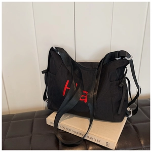 Close-up of black nylon tote bag featuring red embroidered letters and wide shoulder strap