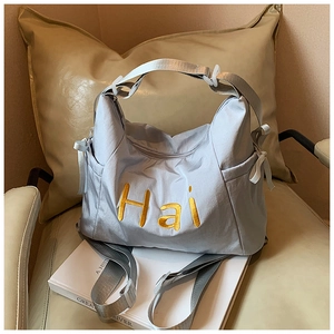 Detail of light blue nylon tote bag featuring yellow Hai embroidery and side pocket