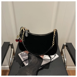 Détail du sac demi-lune en suédine noire avec chaîne dorée et cerise rouge