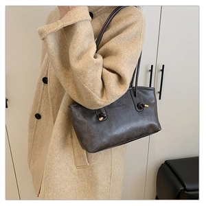Detail of dark grey tote bag with knotted strap and gold metallic accents on a wool coat