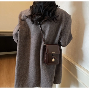 Vertikale bordeauxrote Leder-Handytasche mit goldener Ringschnalle über grauem Blazer