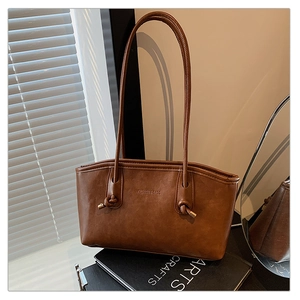 Detail of dark brown leather tote bag with unique knotted handles and gold embossed logo