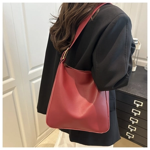 Side view of a red matte leather hobo bag on a model wearing a black blazer jacket