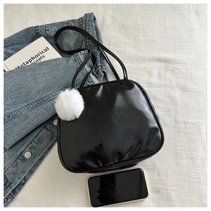 Glossy black leather shoulder bag with white pompom pendant and phone for size reference