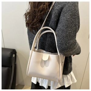 Model wearing a minimalist cream bucket bag with an adjustable crossbody strap and magnetic clasp