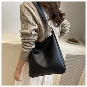 Detail of black minimalist bucket bag with wide strap and gold hardware on model