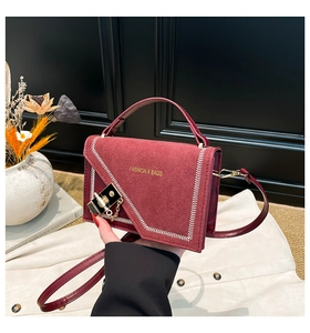 Detail of burgundy leather square bag with white stitching and gold metal lock clasp