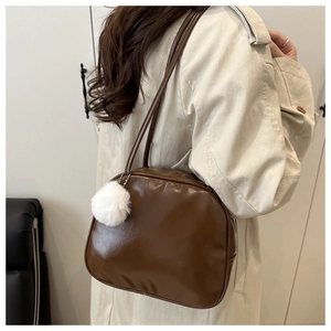 Brown PU leather crossbody bag with white fur pompom shown on model in cozy setting
