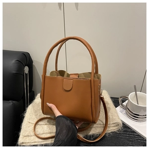 Detail of a brown leather bucket bag with top handles and adjustable strap on a soft knit