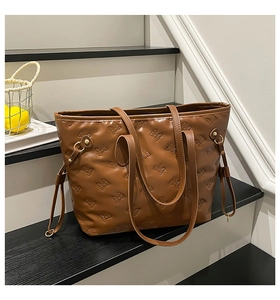 Detailed close-up of brown tote bag with embossed bow pattern on textured leather surface
