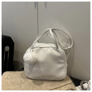 Detail view of a white faux leather pillow bag with a plush fur ball charm on soft rug
