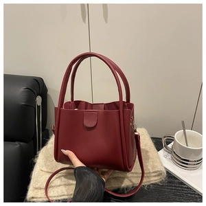Detail of a dark red bucket bag with fixed handles and a round buckle on a beige mat