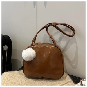 Detail shot of brown glossy PU leather handbag with white faux fur ball keychain