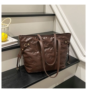 Macro shot of brown tote bag featuring detailed bow embossing and gold metal hardware
