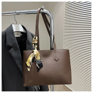 Detail of deep brown leather tote bag featuring a decorative patterned silk scarf handle