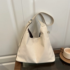 Minimalist cream faux leather hobo tote bag with wide strap on a wooden table