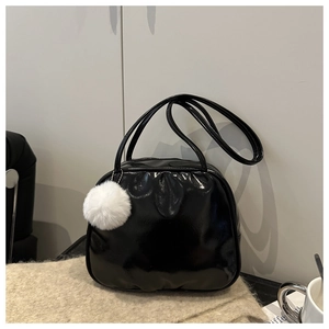 Glossy black pillow bag with dual handles and white plush fur ball detail on soft rug