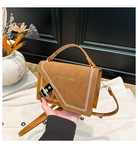 Detailed shot of brown suede crossbody bag with white baseball stitching and metal lock