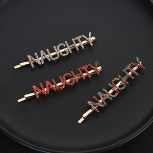 Trois barrettes en alliage doré avec strass colorés épelant NAUGHTY sur fond noir