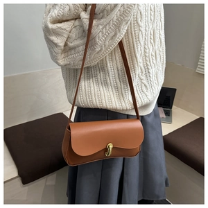 Brown leather crossbody bag with oval gold clasp worn by model in casual interior