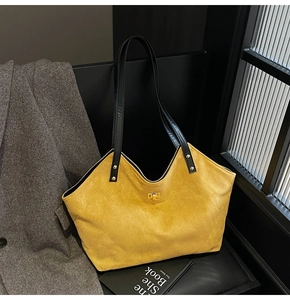 Détail d'un sac cabas en daim jaune matelassé avec boucle dorée et anses en cuir noir