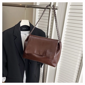 Gros plan d'un sac à bandoulière marron foncé en cuir froissé avec une chaîne argentée