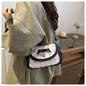 Detail of crossbody bag with floral bow print and heart pendant worn by a model