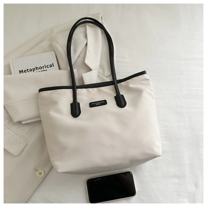 Minimalist white nylon tote bag detail with black slim handles and rubberized logo label