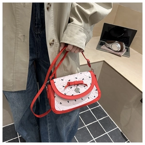 Detail of red bow and heart pendant on white textured crossbody bag with bow pattern