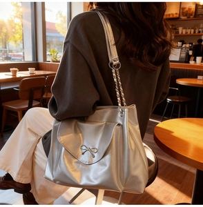 Close-up of metallic silver tote bag with bow detail and chain strap on female model