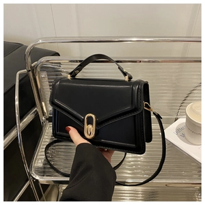 Detail of black leather crossbody bag with golden oval twist lock on a silver metal stand
