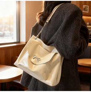 Detail of cream tote bag featuring silver bow ornament and elegant chain strap texture