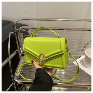 Detail of neon green square handbag featuring a gold oval lock and top handle