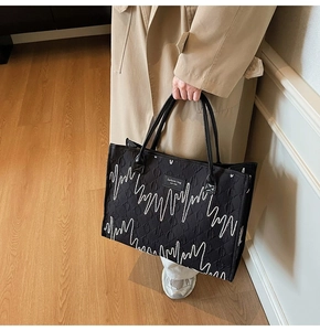 Detail of black quilted tote bag with wavy embroidery and leather handle on a model