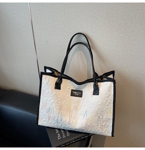Detail of colorful wavy embroidery and black leather trim on a white canvas tote bag