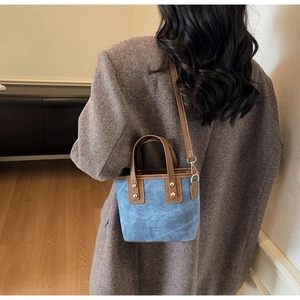 Detail of blue and brown bucket bag with gold rivets and detachable strap shown on model