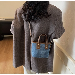 Detail of blue canvas bucket bag with brown leather trim and gold rivet handle