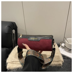 Detail of burgundy suede cylinder bag with a wide ethnic patterned strap and gold hardware